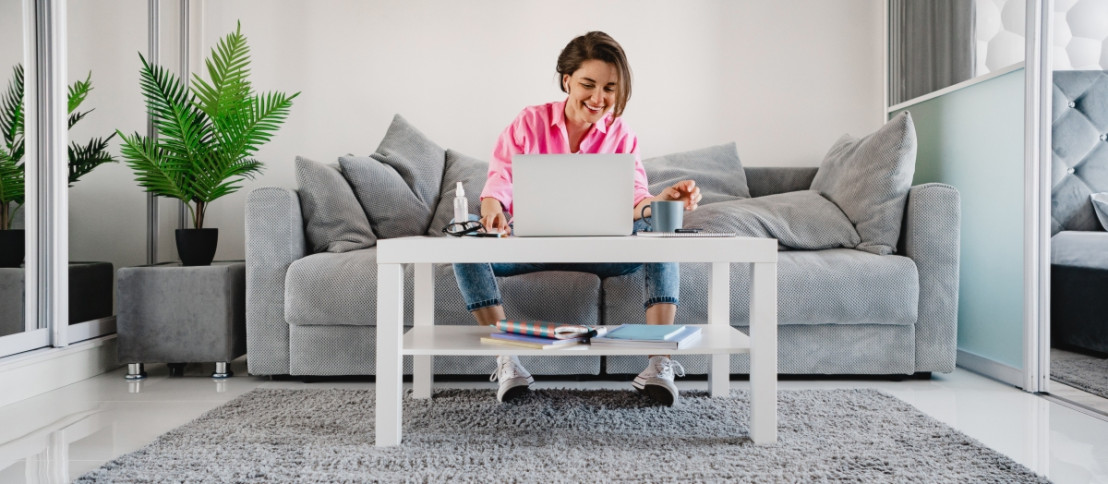 Vrouw vult enquêtes in vanuit de woonkamer op de bank en doet dat op een laptop