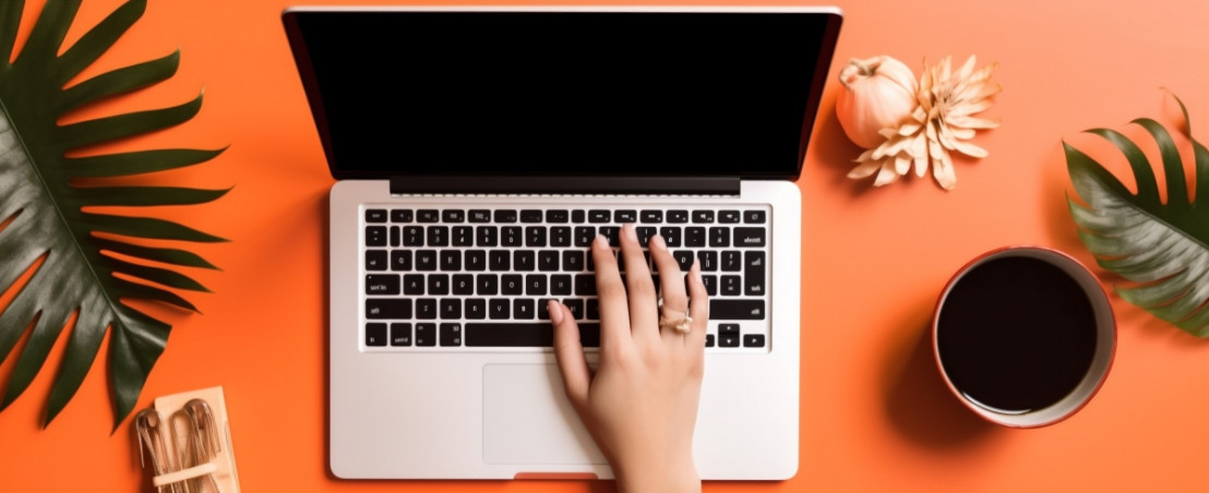 Laptop, koffie en een groene tak met daarachter een oranje achtergrond als thuiswerkplek